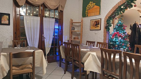 La sala della trattoria con l'arco in mattoni e i quadri alle pareti