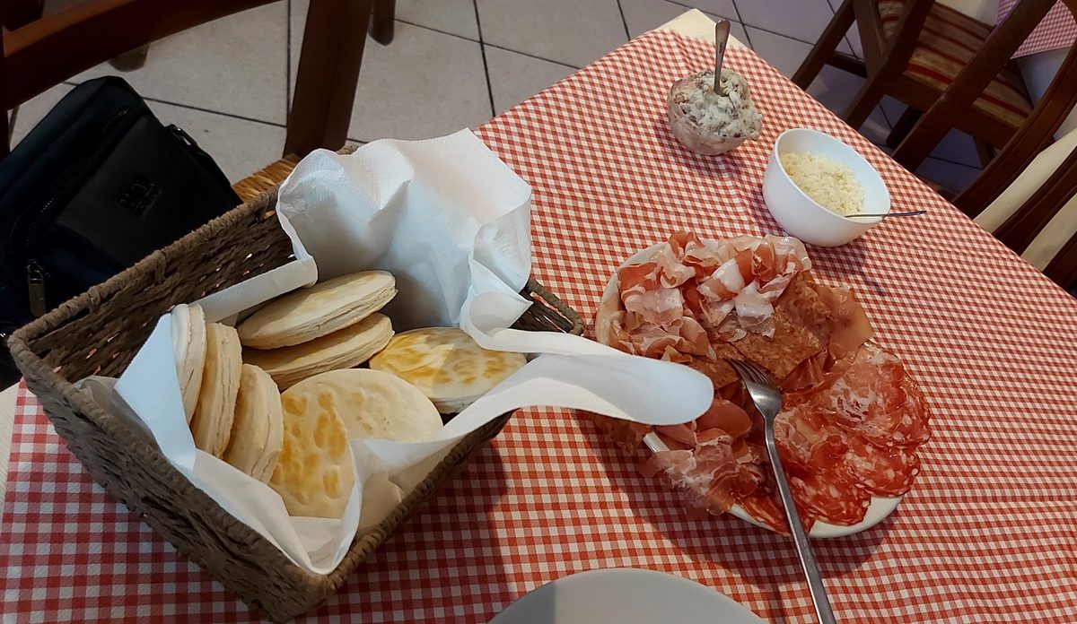 Cestino di tigelle appena cotte accanto a un piatto di affettati misti